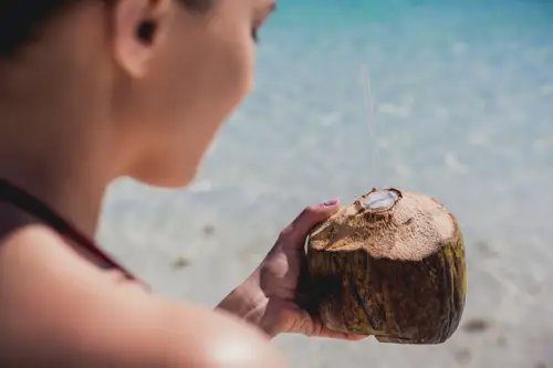 A woman on the beach holds a coconut